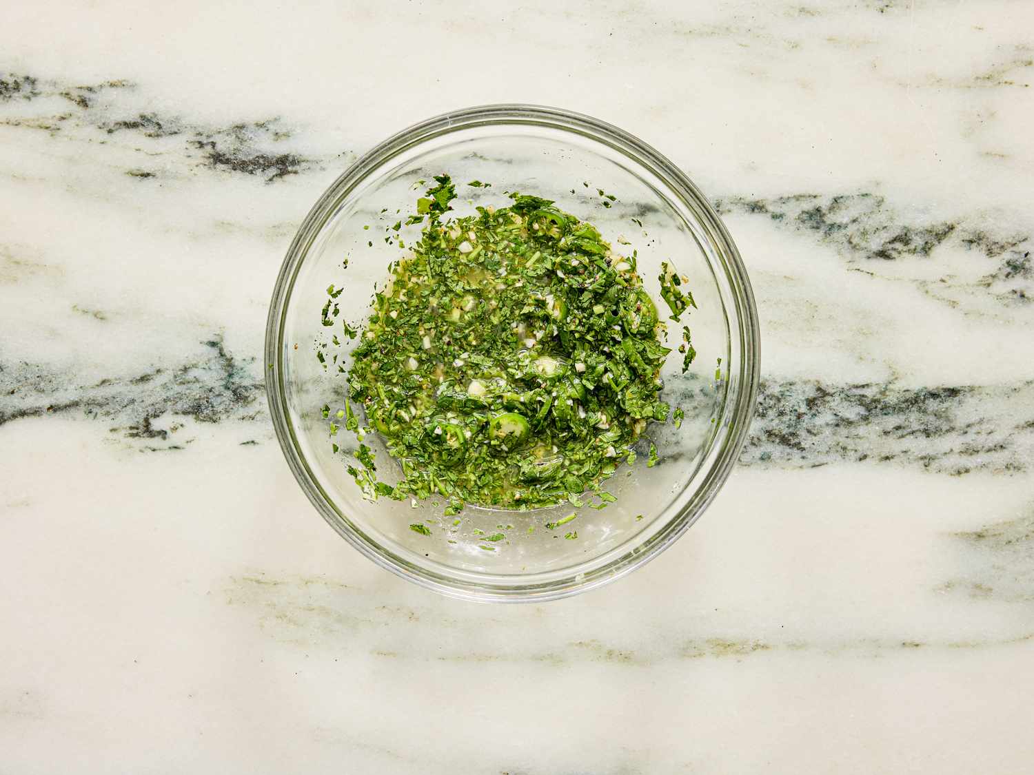 A bowl of chopped green herbs or salad on a marble countertop