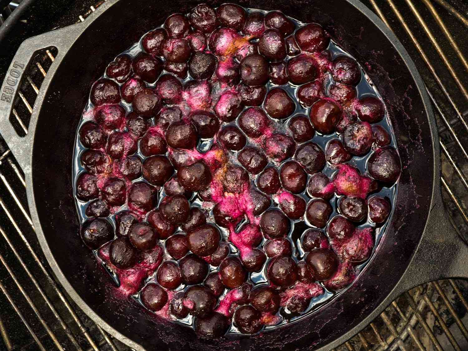 A cast iron skillet of roasted cherries on a grill.