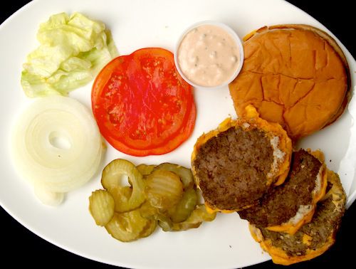 Overhead view of the components of a cheese burger from In-n-Out, disassembled and laid out on a white platter.