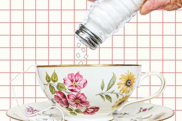 Table salt being added to a porcelain teacup covered with flowers.