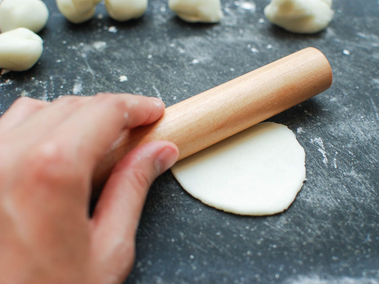 Author rolling out a piece of dough into a thin disk-shaped wrapper with a small roller.