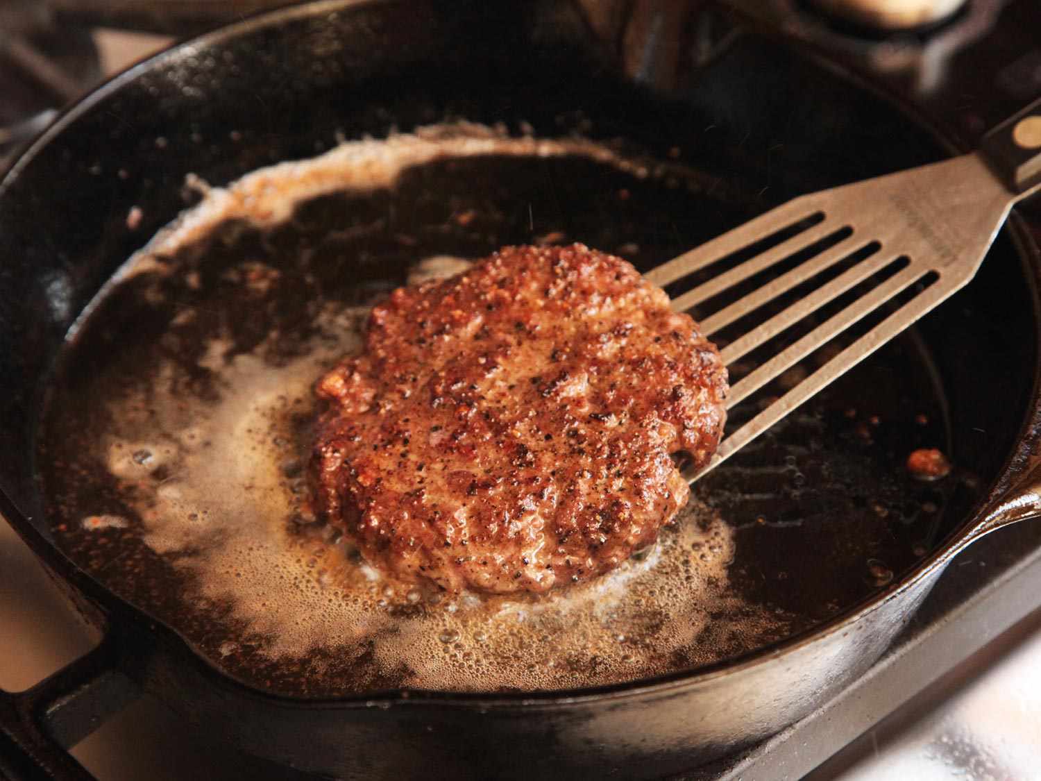 Searing a sous vide hamburger in oil in a cast iron skillet with a fish spatula.