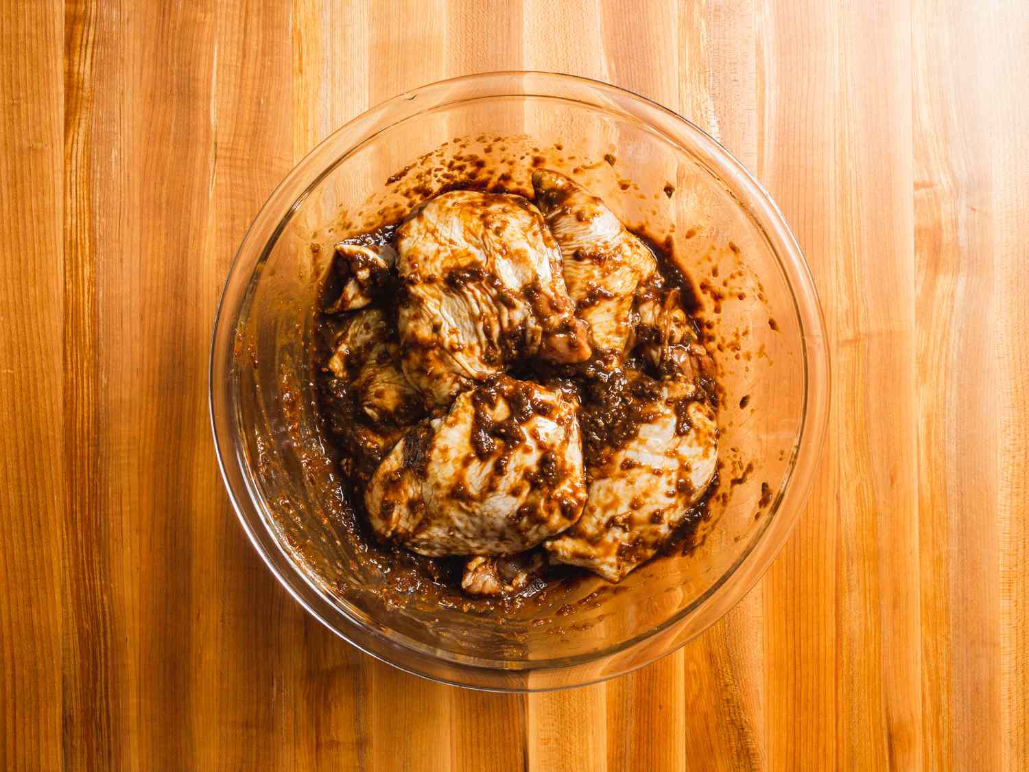 Overhead view of the marinated chicken in a pyrex bowl on a wooden countertop.