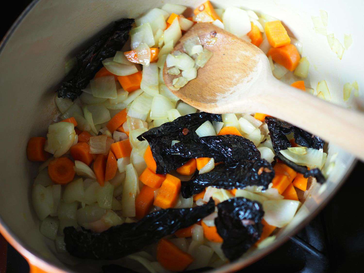 Stirring onion, roasted butternut squash, and ancho chiles in a Dutch oven for soup. 