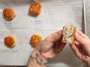Hands holding a halved fried potato patty with several patties on a marked baking sheet in the background