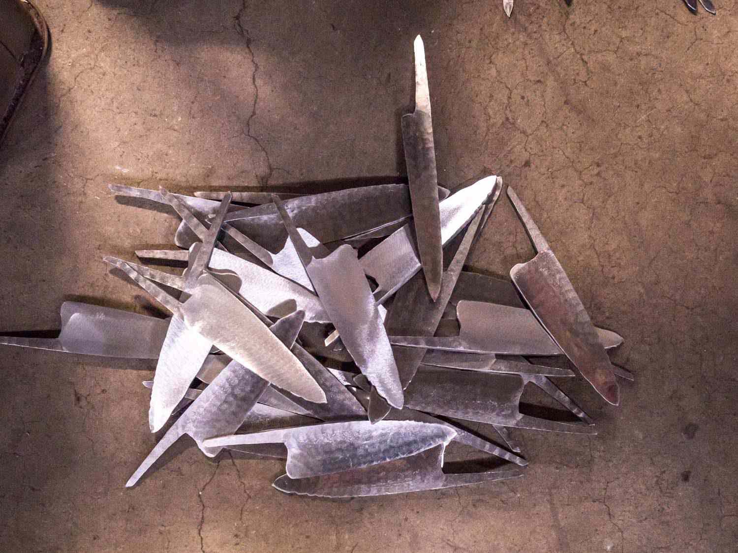 A haphazard pile of ground gyuto kitchen knife blanks strewn on a concrete floor.