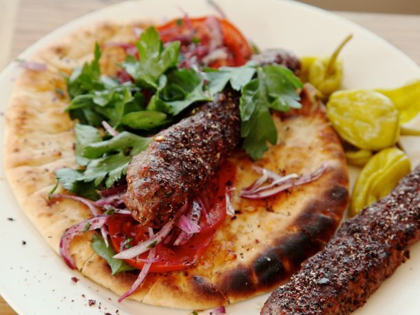 Finished Adana kebab, plated on a grilled pita with tomato slices, parsley, and red onions.