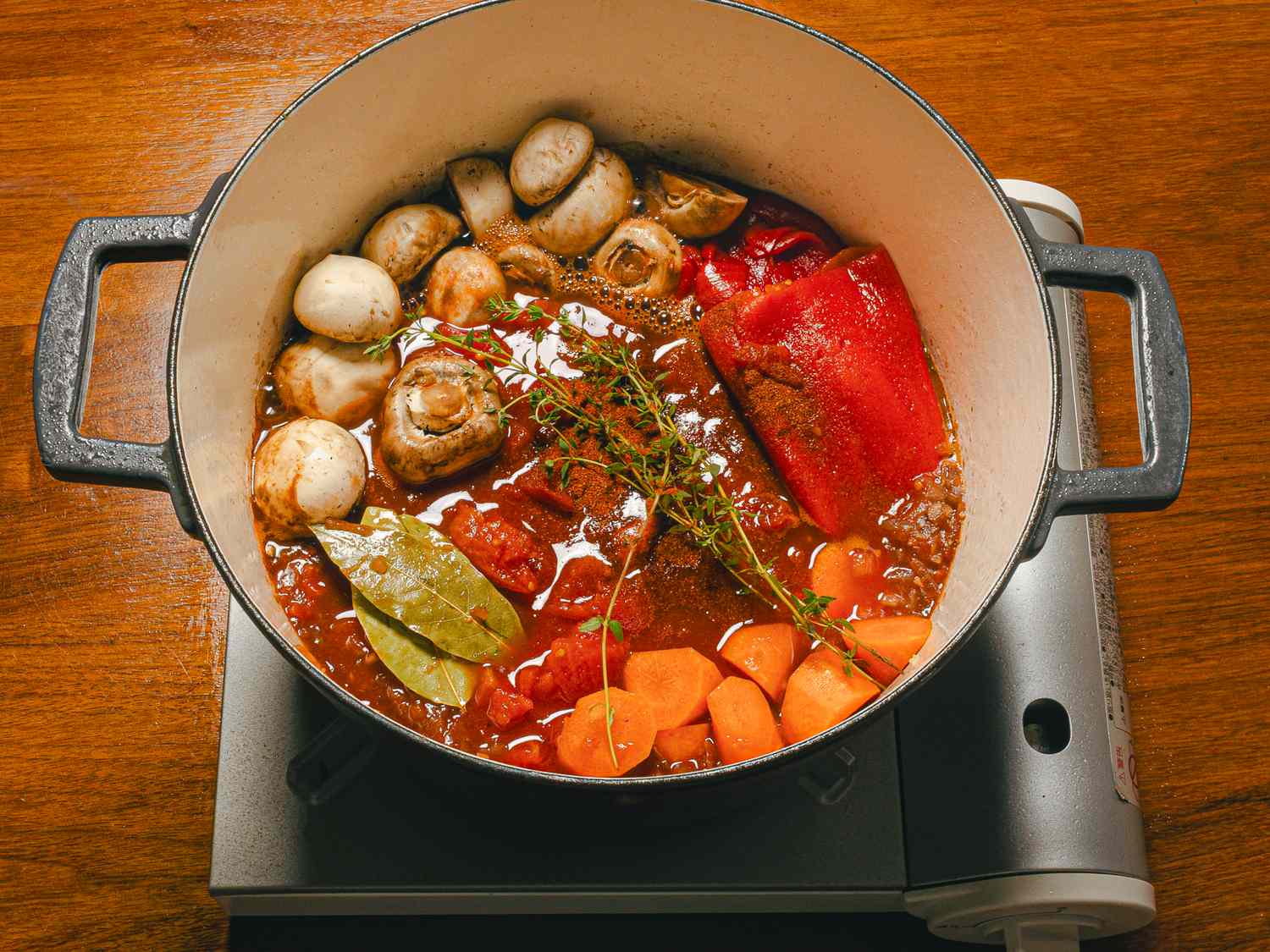 Spanish beef stew in a pot with vegetables and herbs simmering on a burner
