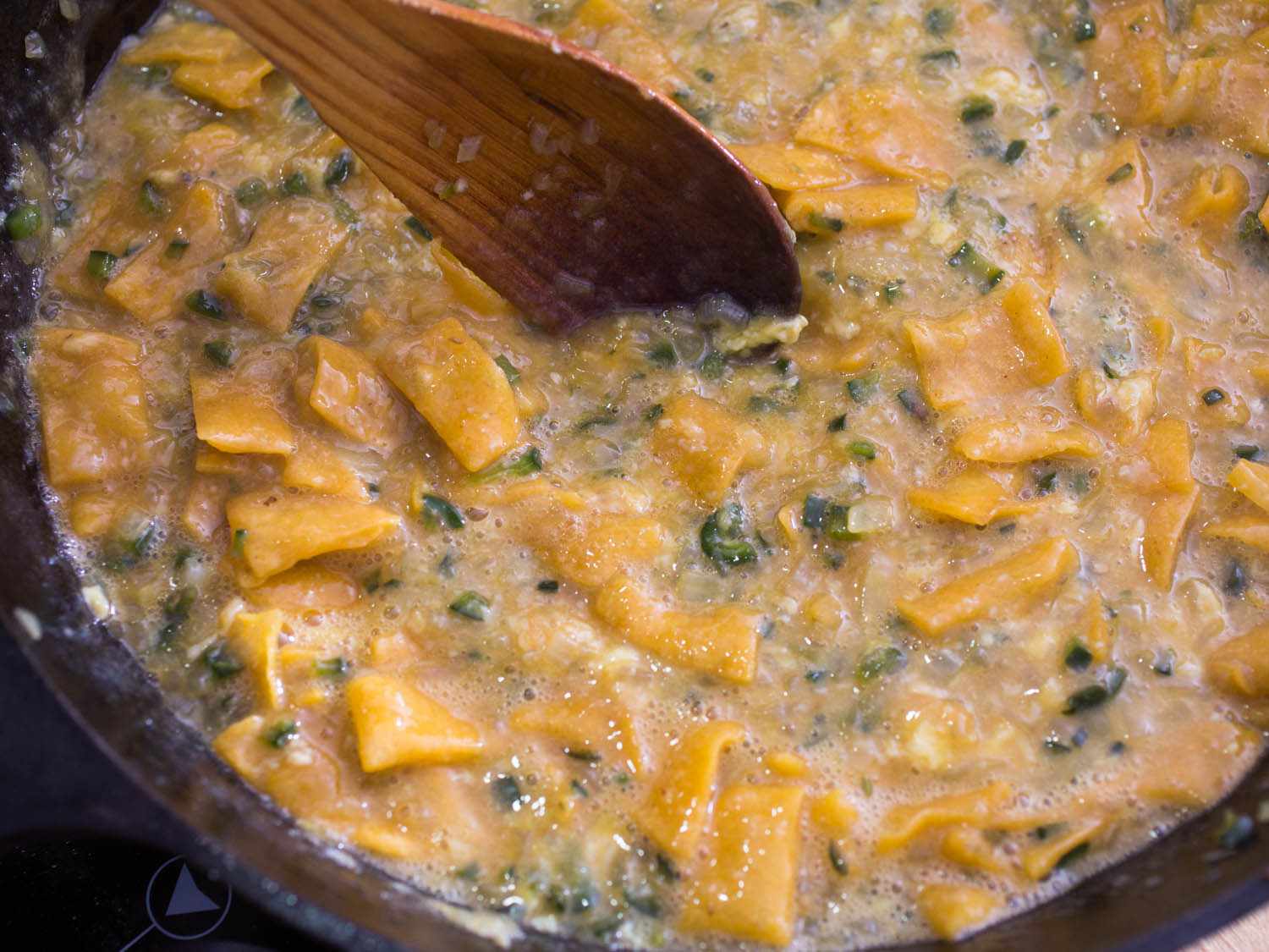 Stirring almost-cooked migas with scrambled eggs, fried chips, and vegetables.