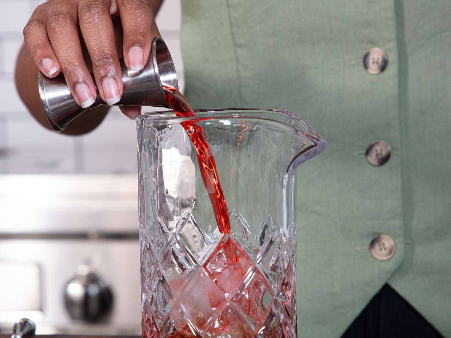 A person pours liquid into a glass pitcher in a kitchen setting