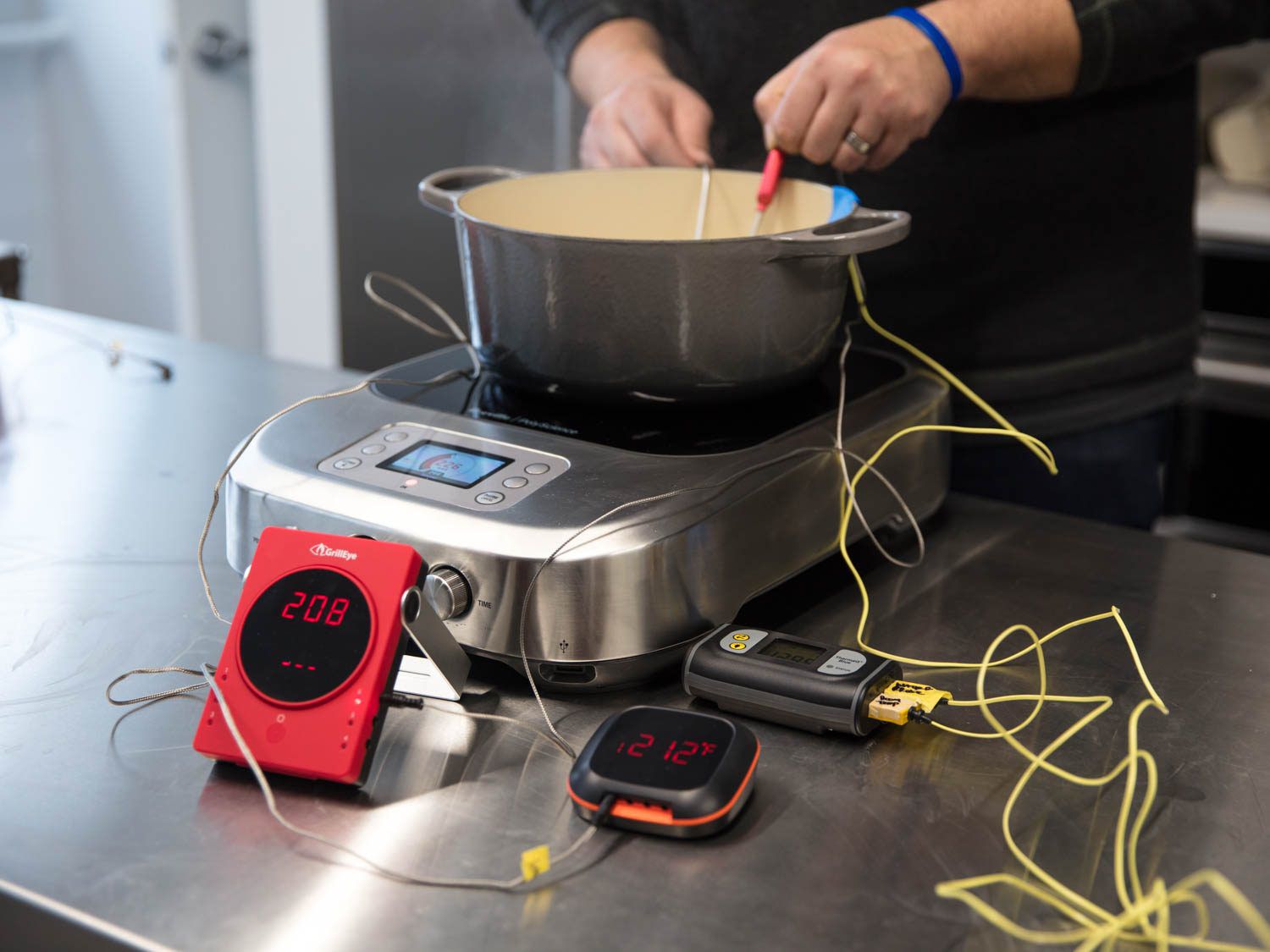 three different thermometers checking the temperature of boiling water in a Dutch oven set on an induction burner