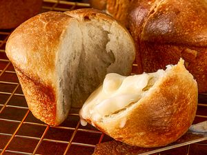 Fresh baked rolls with one cut open and spread with butter arranged on a cooling rack