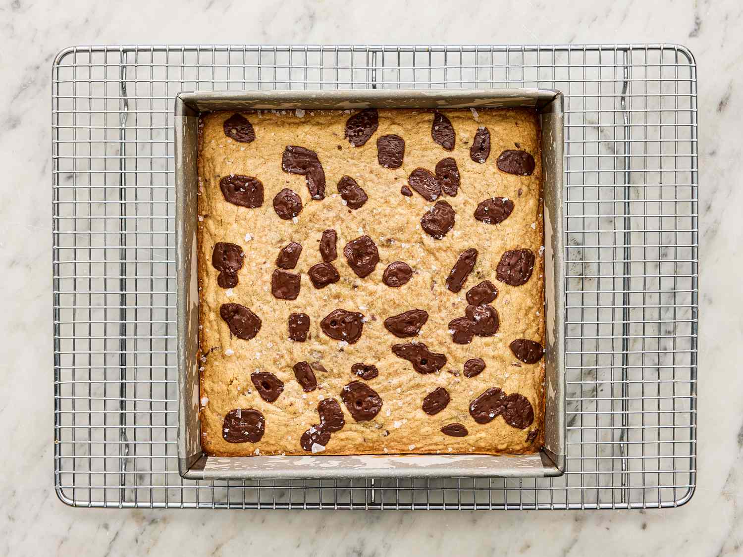 A baked banana bread blondie in a square pan placed on a cooling rack