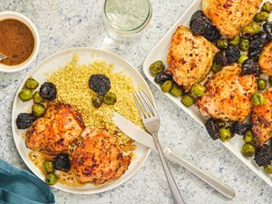 A dish of roasted chicken thighs with prunes olives and couscous on a plate and serving tray