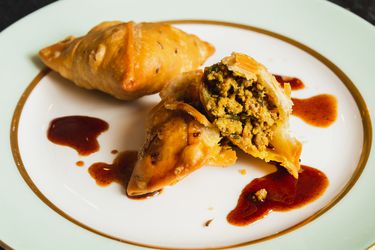 Two kheema samosas on a plate, one broken open to show its interior.