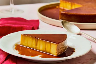A slice of orange and saffron flan on a plate with caramel sauce placed beside a full flan serving in the background