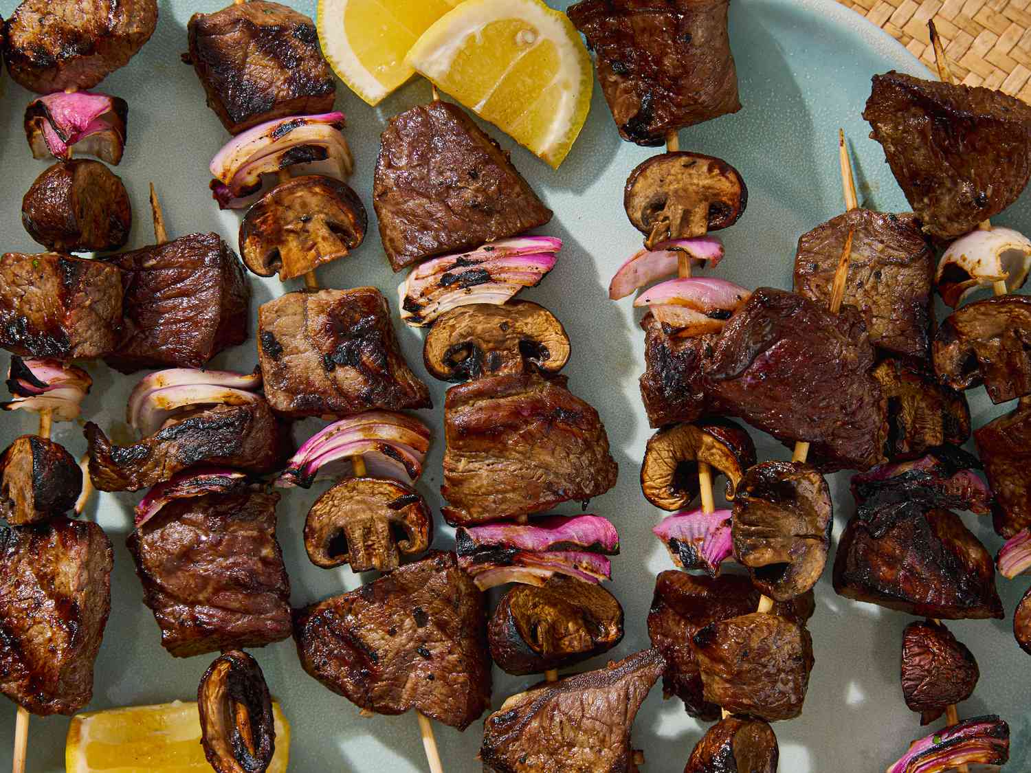 Grilled kebabs with steak, mushrooms, and onions on skewers on a plate with lemon slices