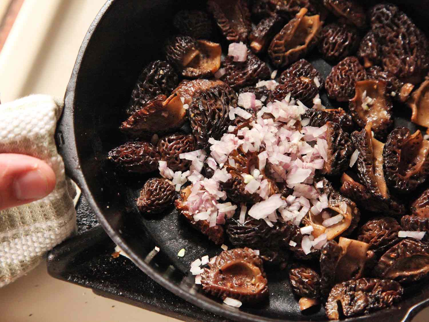 Minced shallot in a skillet with sautéed morel mushrooms.