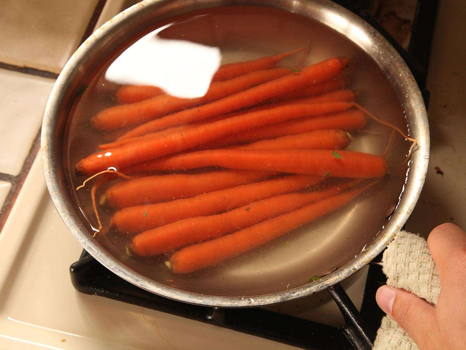 Whole carrots covered with water in a skillet.