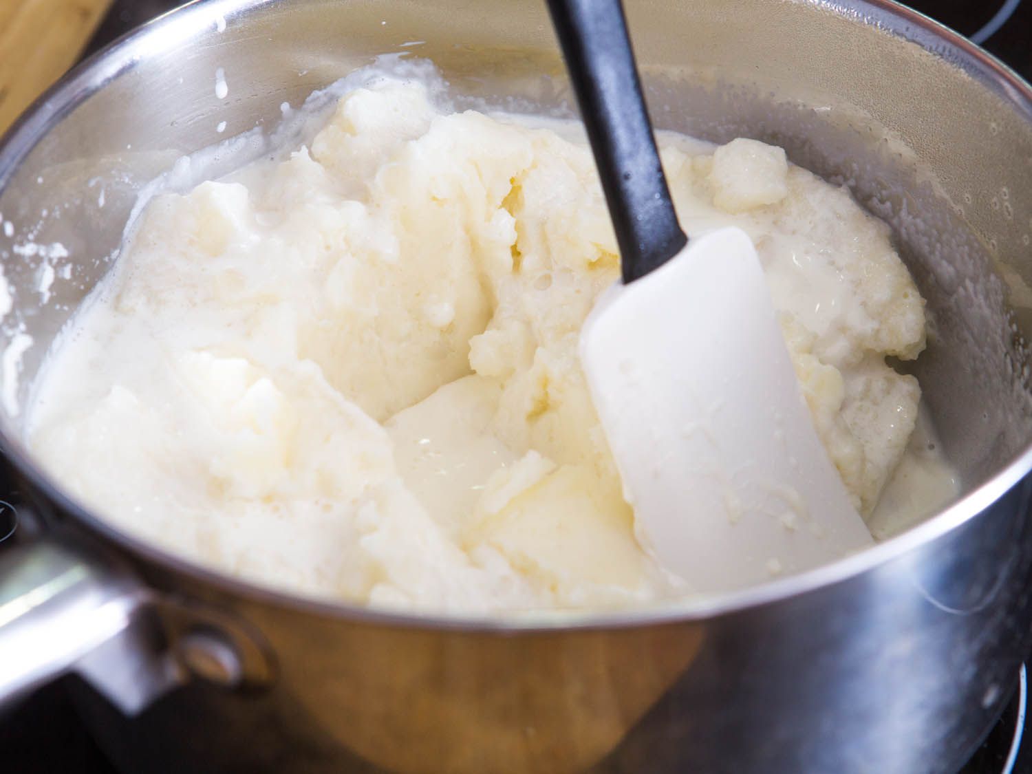 Mashed potatoes, liquid, and butter being stirred together with a silicone spatula.