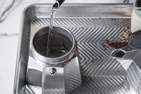 A person pouring water into the base of the Bialetti Moka Express moka pot.
