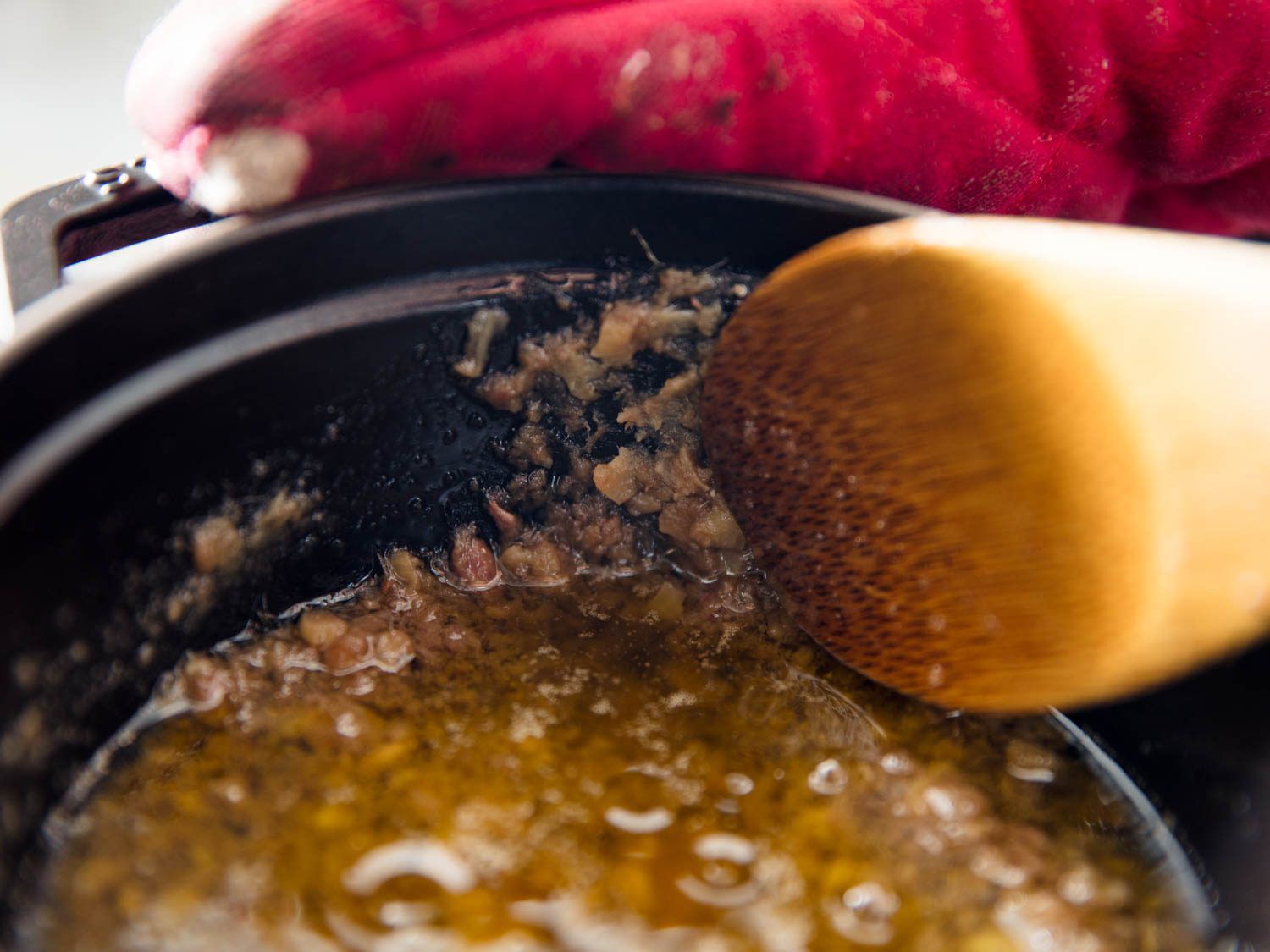 A wooden spoon smashing bits on the side of a pot full of anchovies.