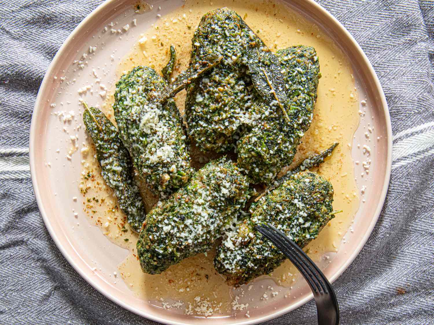 A plate of stuffed green peppers garnished with grated cheese and served on a textured surface