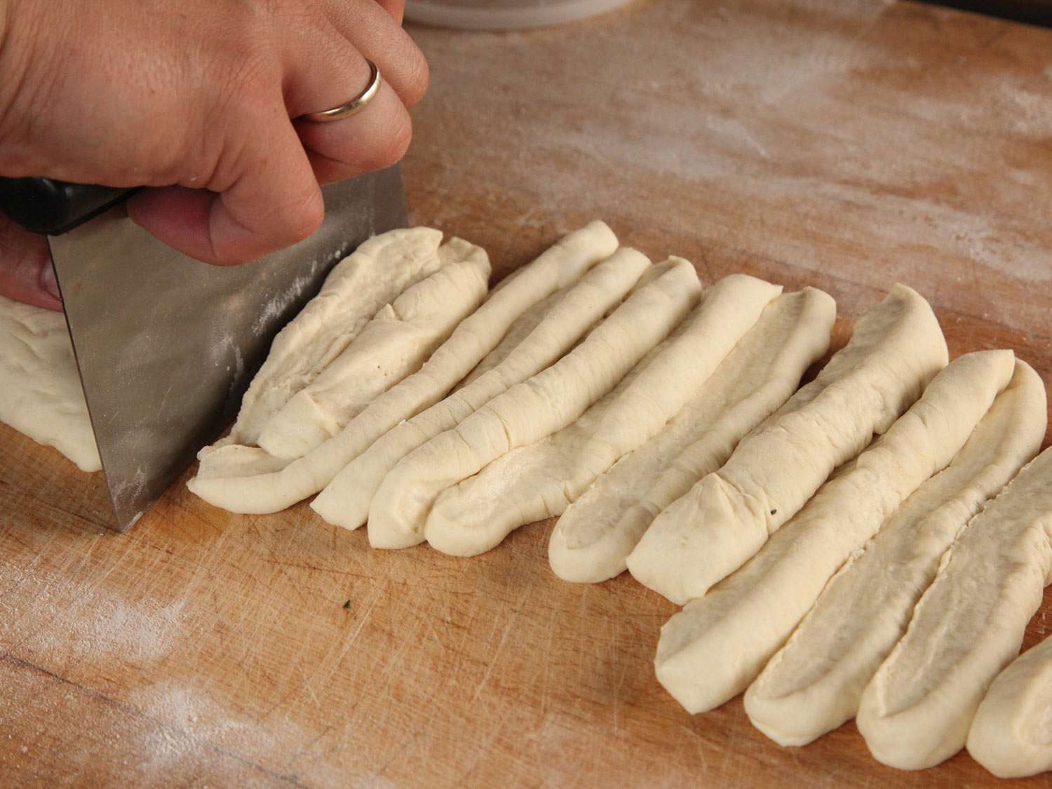 Using a bench scraper to cut a rectangle of dough into long strips