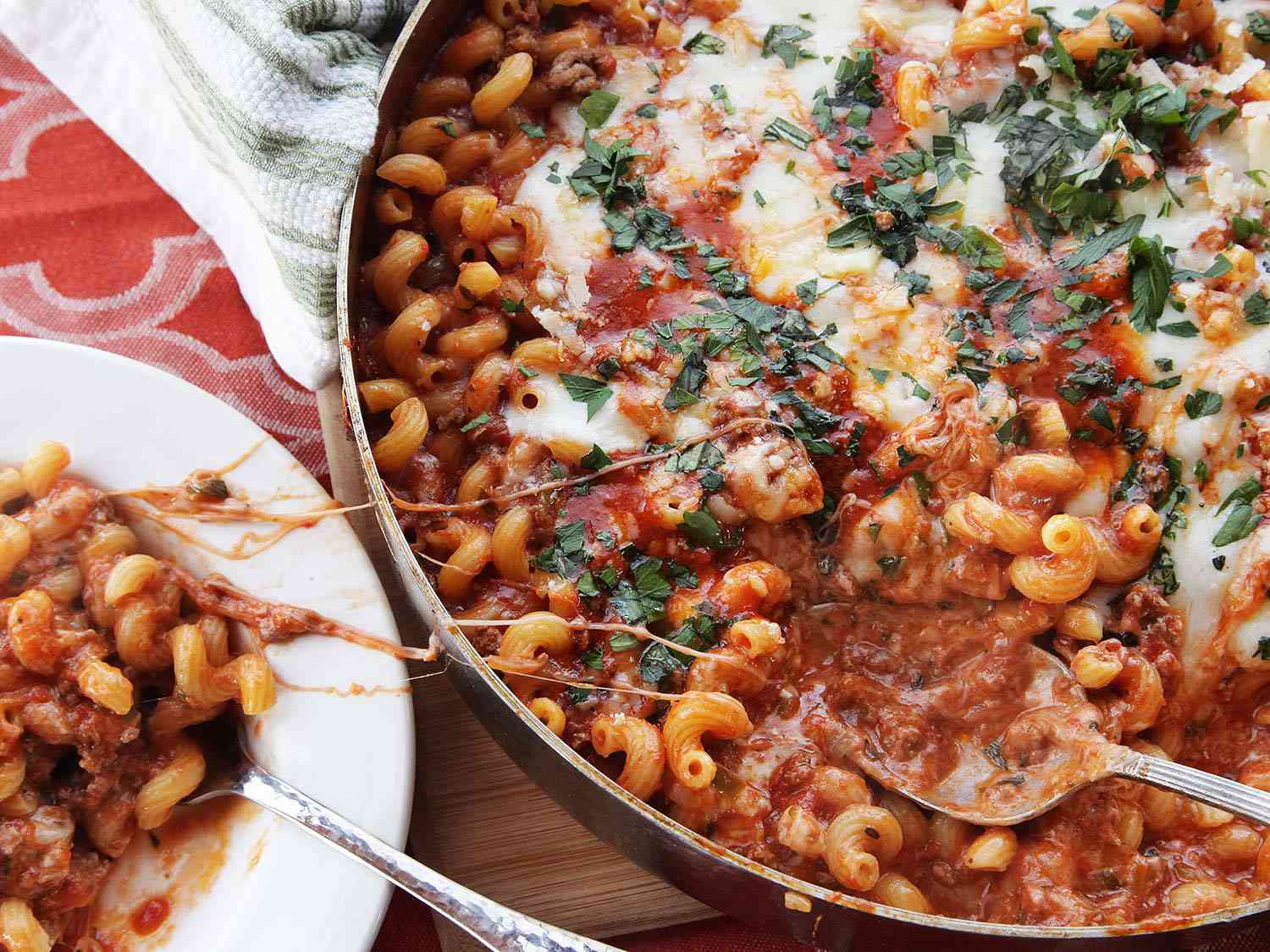The finished casserole with a plate next to it. A healthy spoonful of the pasta has been transferred to the plate, leaving a trail of molten mozzarella.