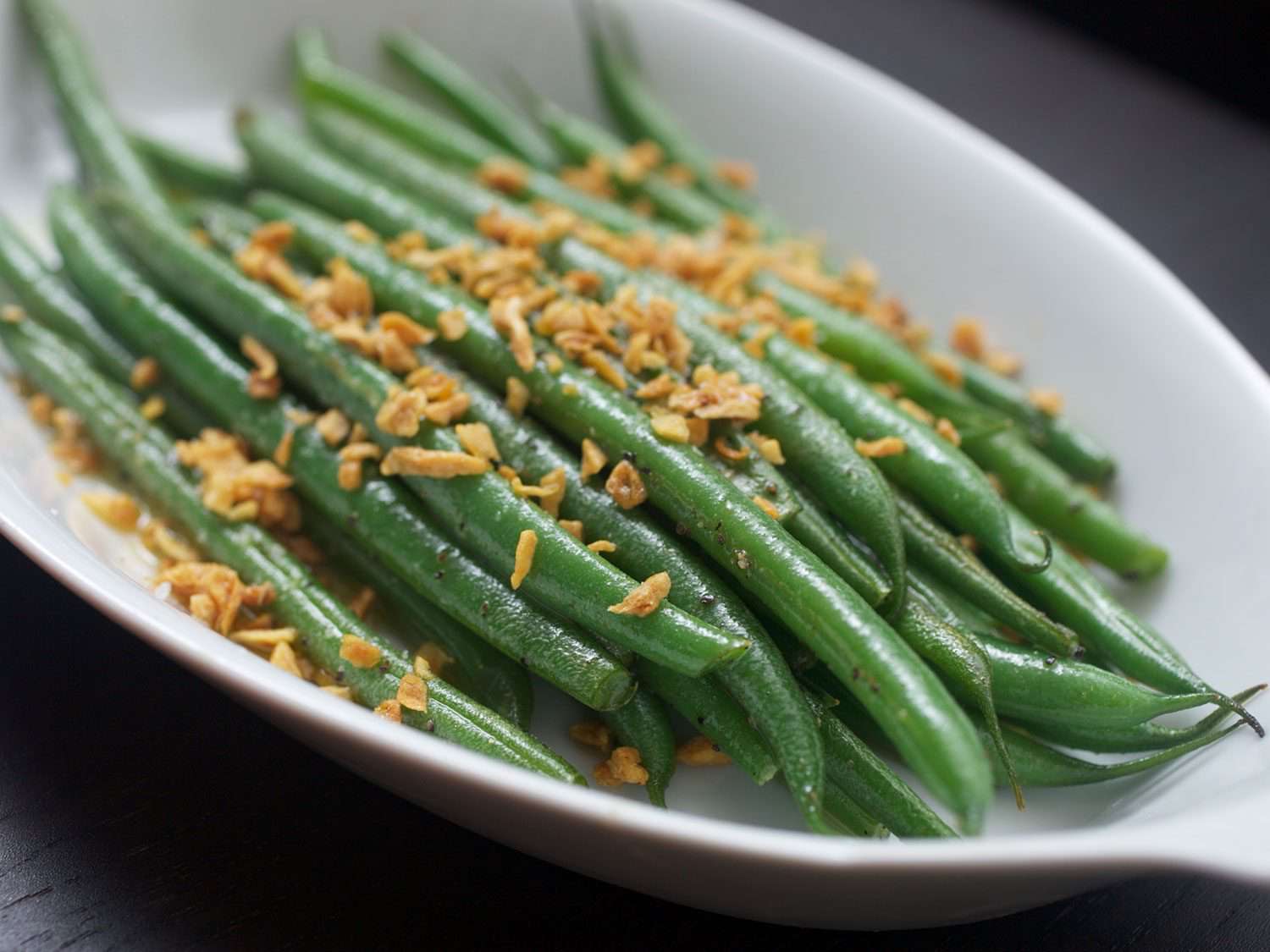 Green beans in a serving dish, topped with fried garlic.