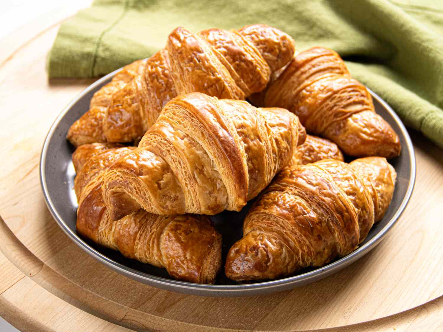Plate of croissants arranged on a wooden surface with a green cloth in the background