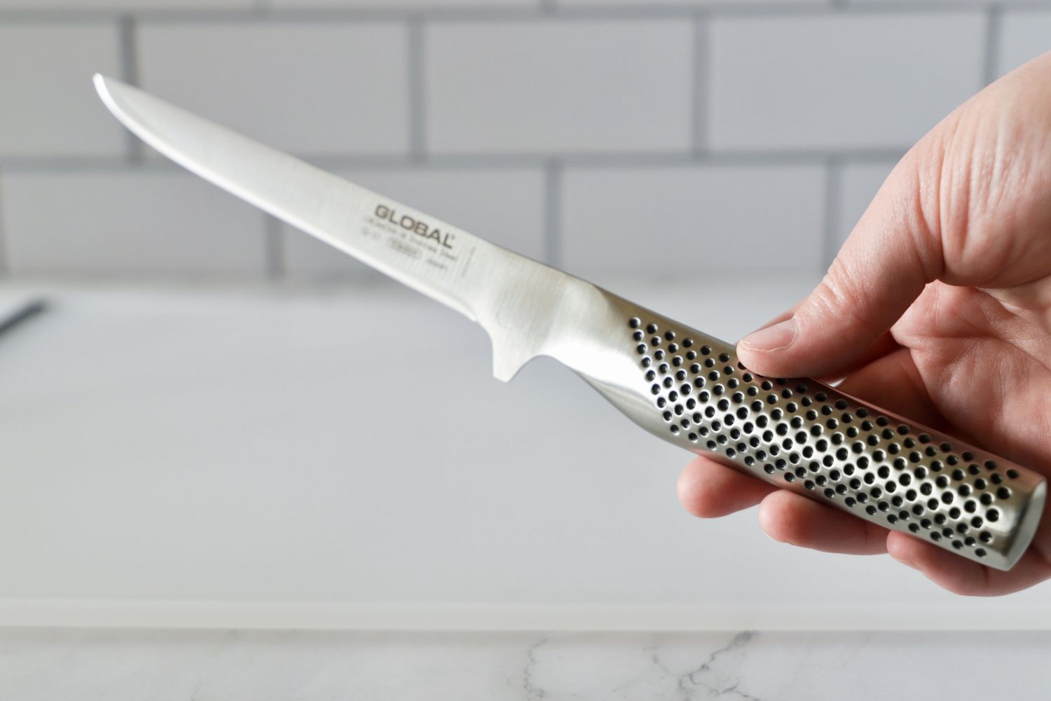 A person holding the handle of the Global boning knife.