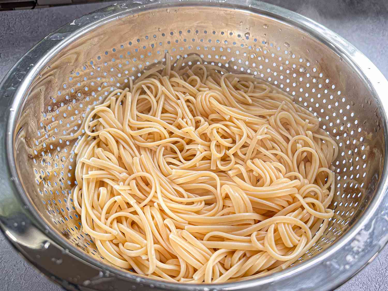 Cooked spaghetti draining in a metal colander