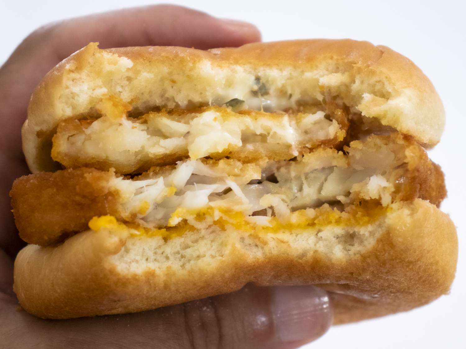 Hand gripping a Mcdonald's Filet-O-Fish with a hash brown slid inside with a large bite taken out of it.
