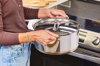 A person lifts the All-Clad Copper Core 10-Piece Cookware Set pot by the handle