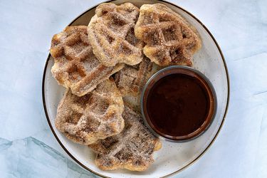 Waffle iron churros with dipping sauce on a plate, on a stone surface.