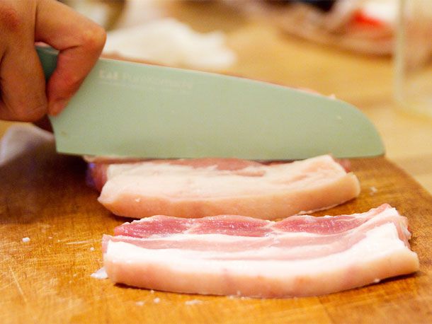 Cutting cured pork belly into 1/2-inch wide strips lengthwise.