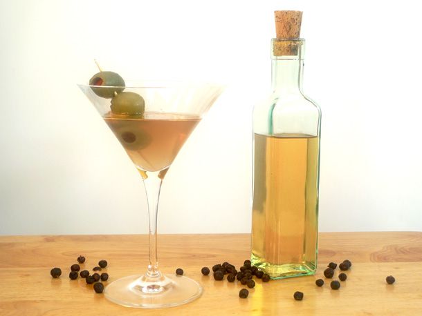 A small bottle of homemade gin flanked by an olive-garnished martini.
