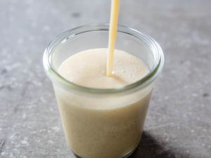 Stream of homemade sweetened condensed milk being poured into glass jar