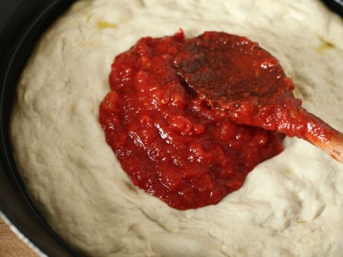 Spreading tomato sauce onto an unbaked pizza dough. 