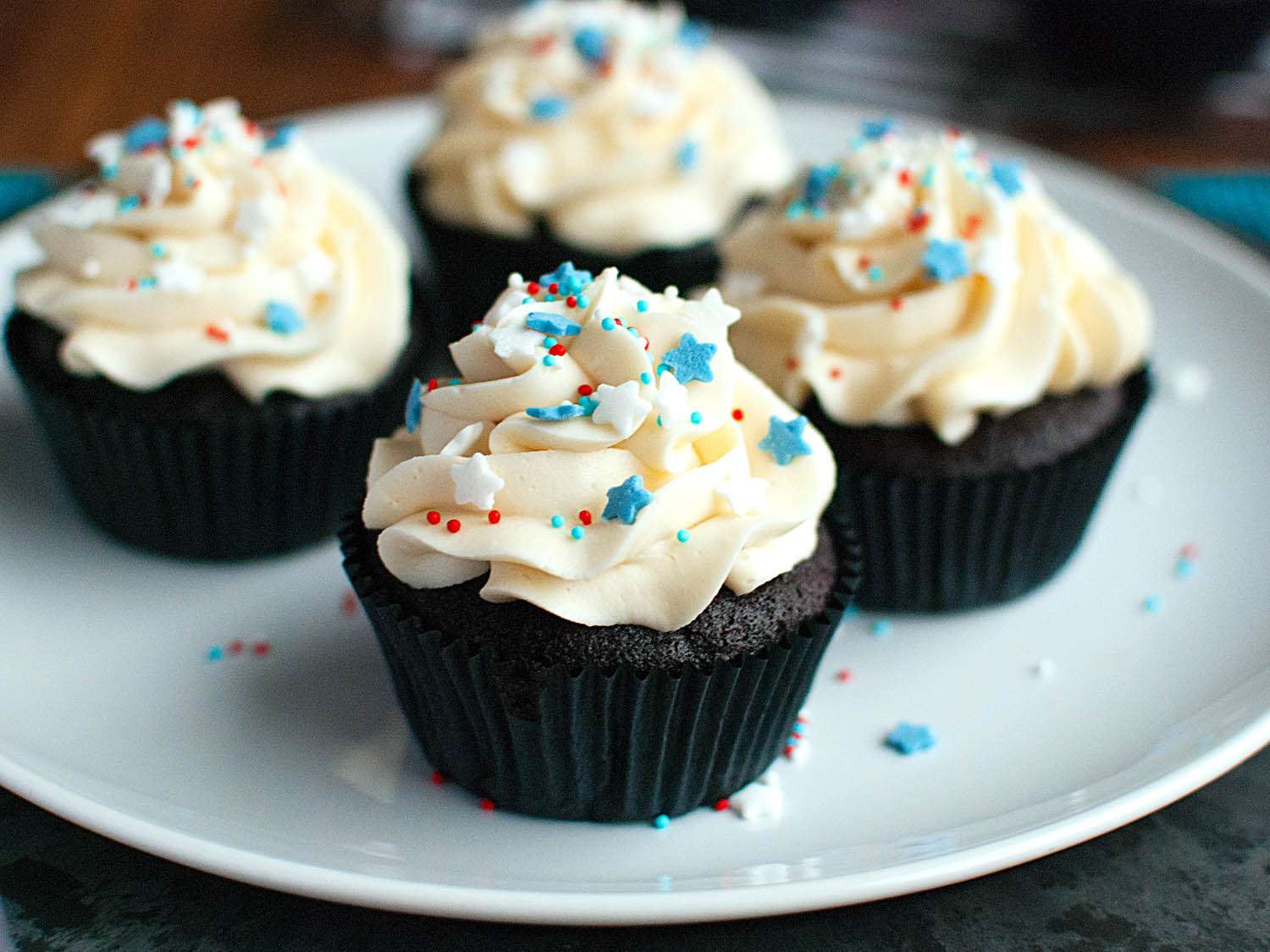 Four American buttercream cupcakes with sprinkles on a plate.