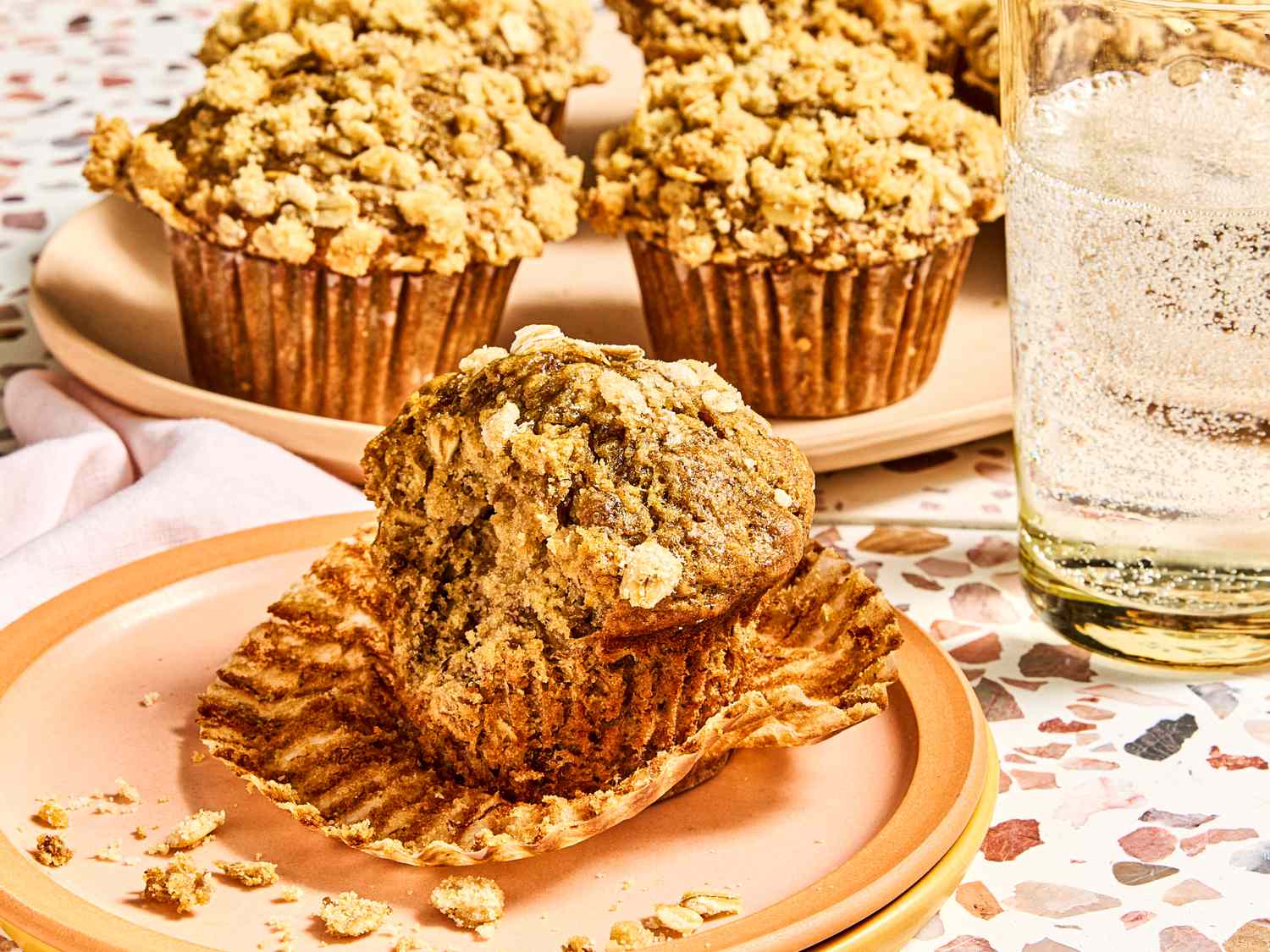 A tray and a plate of banana oatmeal muffins with a glass of sparkling water