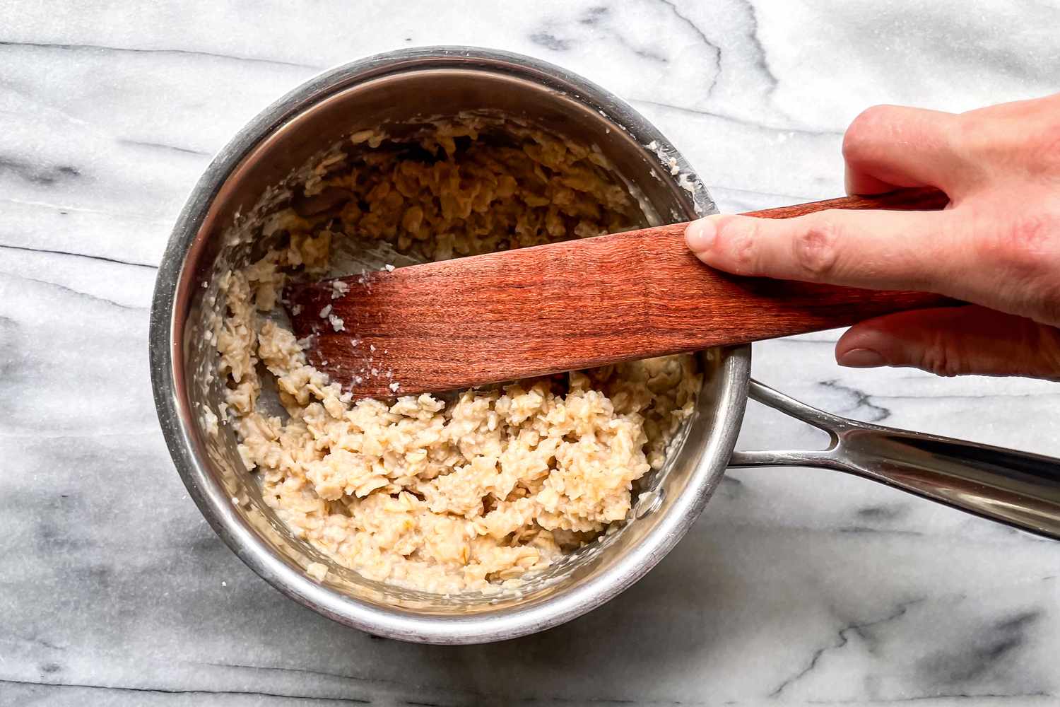 Hand stirring oatmeal in a pot with a wooden spatula