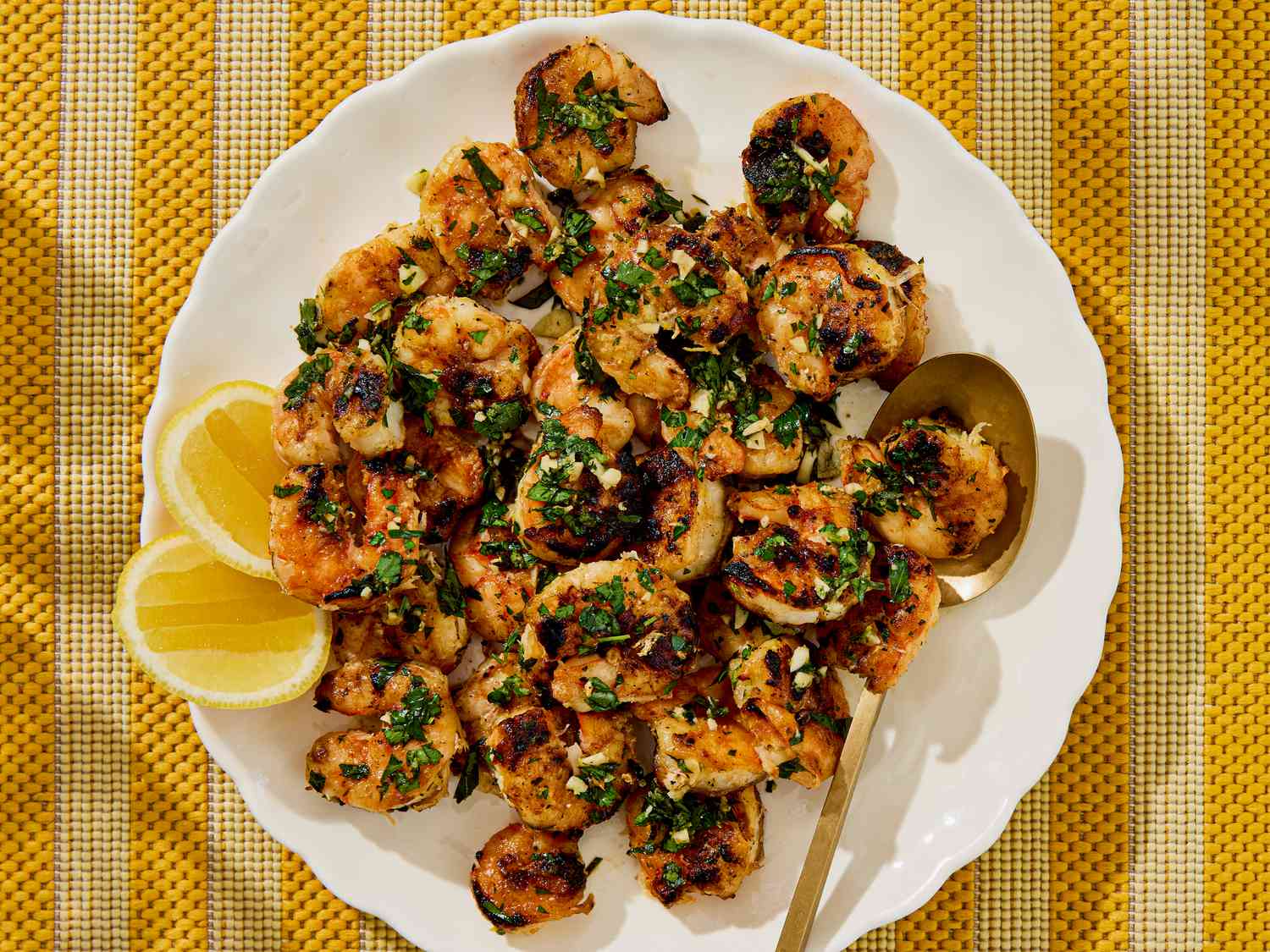 Grilled shrimp garnished with herbs next to lemon wedges on a plate