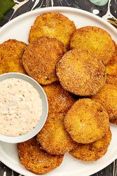 Overhead of Fried Green Tomatoes and dip on a printed surface. Plate on the corner has bitten tomatoes on it