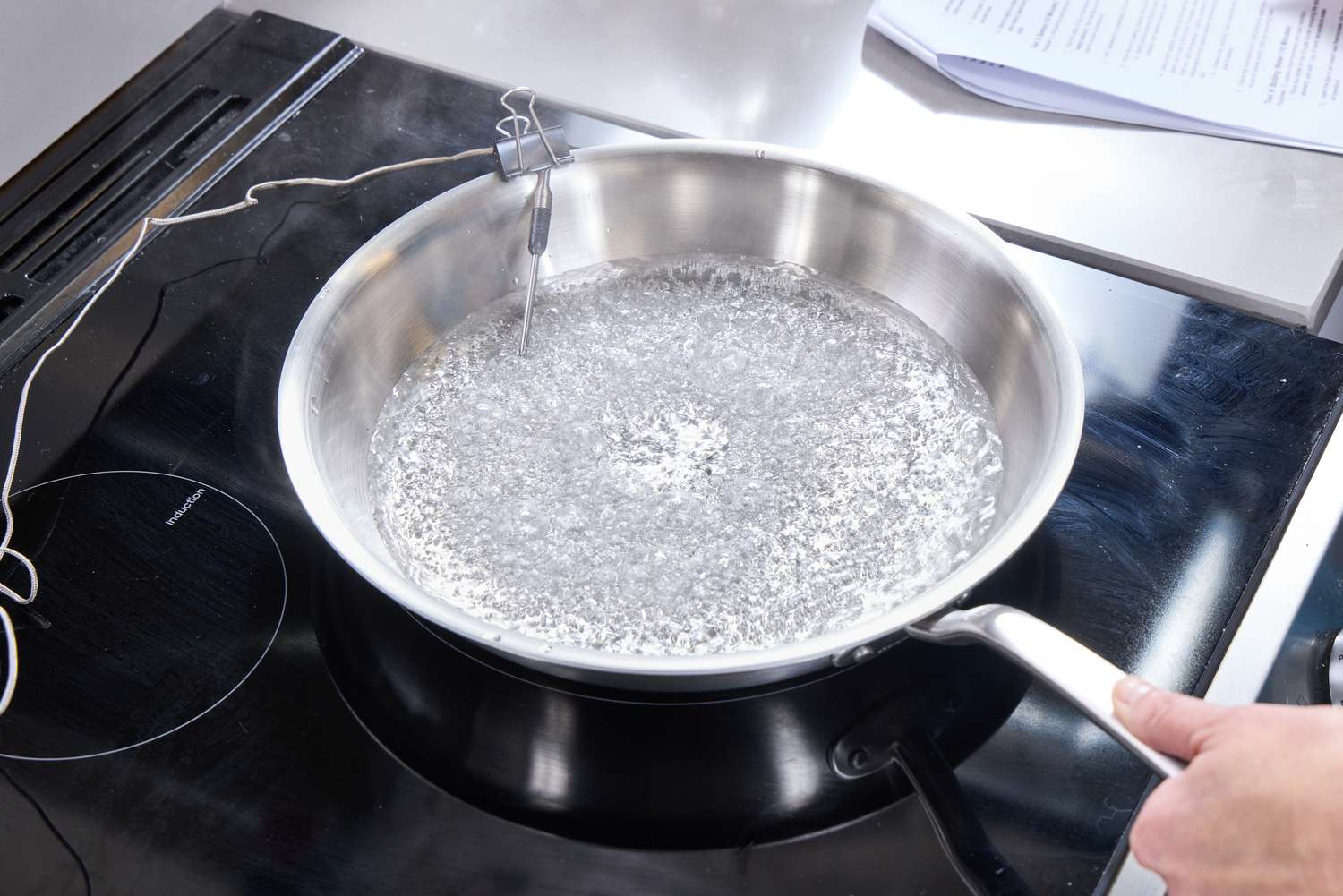 A person boils water in a stainless steel skillet.