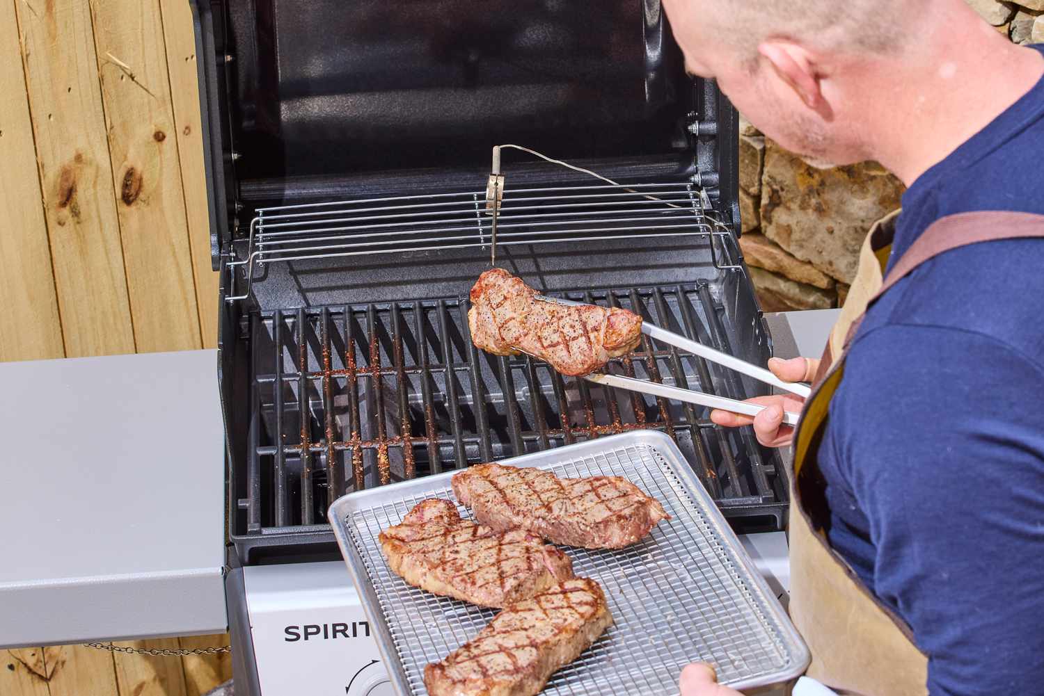 A person using tongs to move steak from the Weber Spirit E-210 Gas Grill to a tray