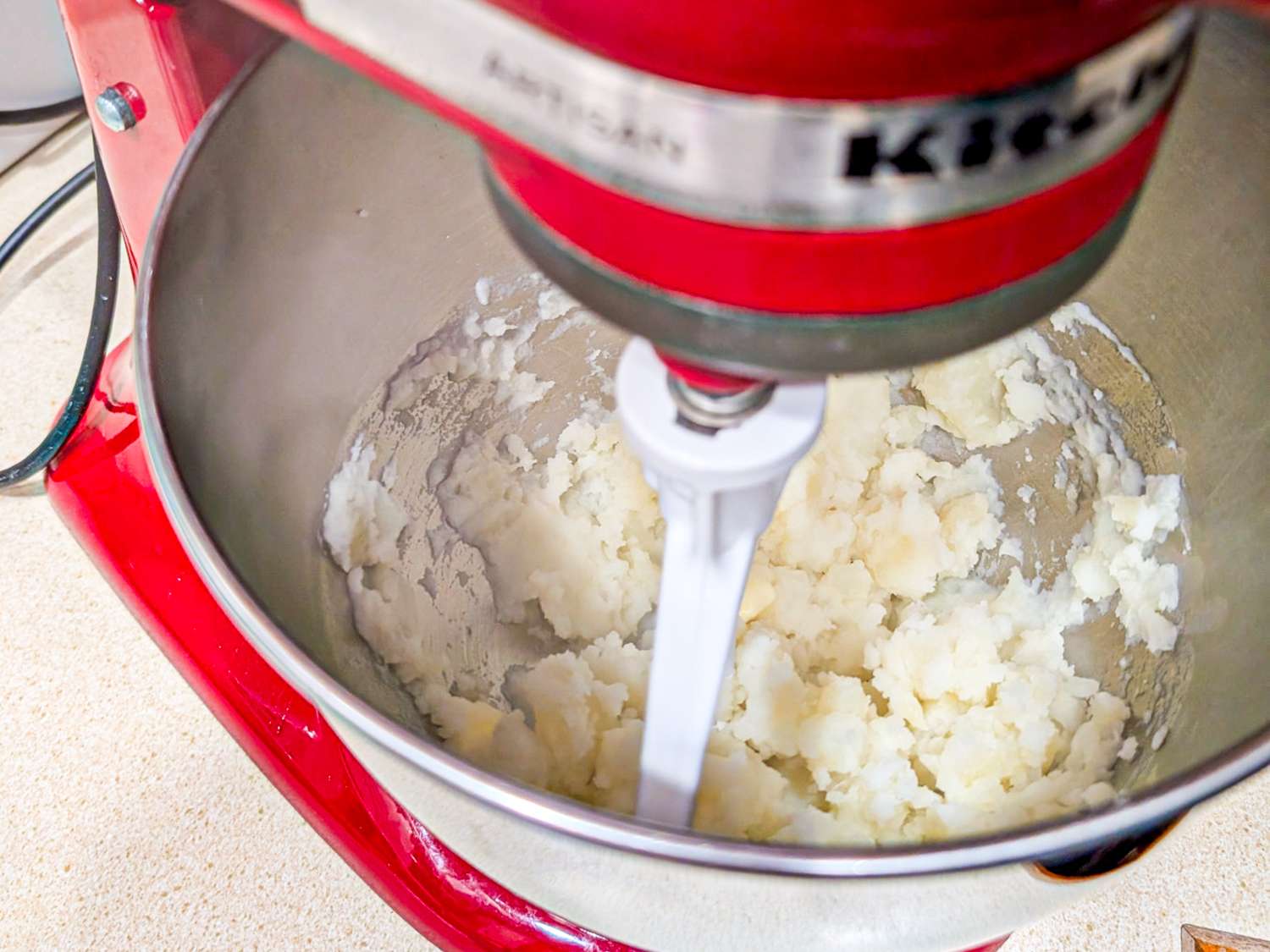 Mixer bowl with mashed potatoes being mixed by a stand mixer paddle attachment