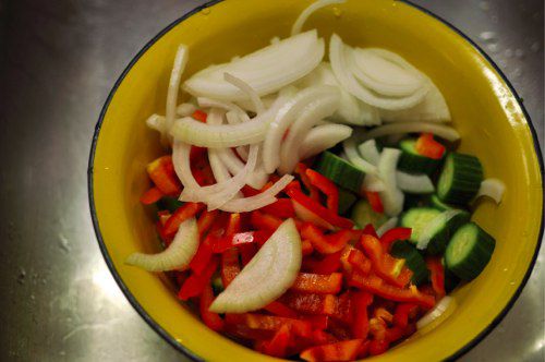 A mix of sliced onion, bell pepper and cucumber in a yellow bowl. 