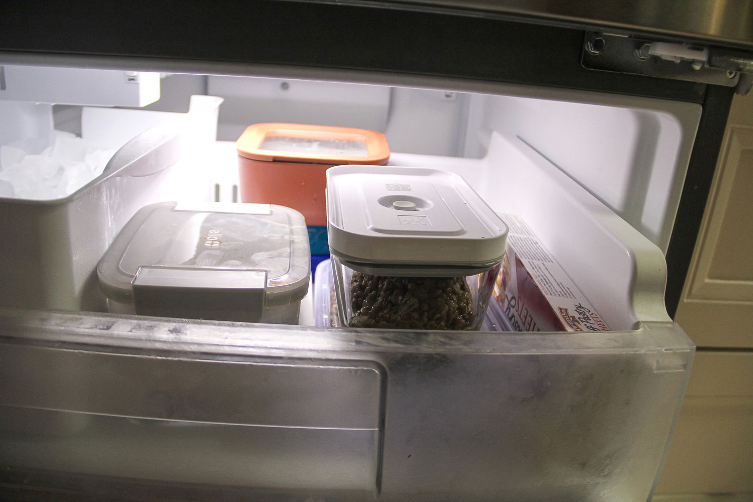 Open freezer drawer with various containers and food items visible